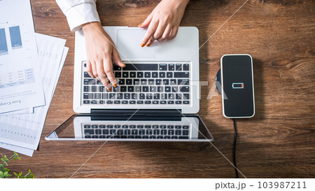 Charging mobile phone battery with wireless charging device in the table. Smartphone charging on a charging pad. Mobile phone near wireless charger Modern lifestyle technology concept. 103987211