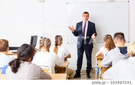 Male teacher at whiteboard during lesson with teen students 103987241