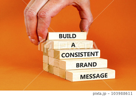 Consistent brand message symbol. Concept words build a consistent brand message on wooden blocks. Businessman hand. Beautiful orange background. Business consistent brand message concept. Copy space. Consistent brand message symbol. Concept words build a consistent brand message on wooden blocks. Businessman hand. Beautiful orange background. Business consistent brand message concept. Copy space. 103988611
