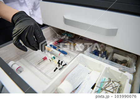 Close-up hand of a dentist in black glove, taking out dental tool form the drawer with dental instruments, consumables and supplies used in a dental practice 103990076