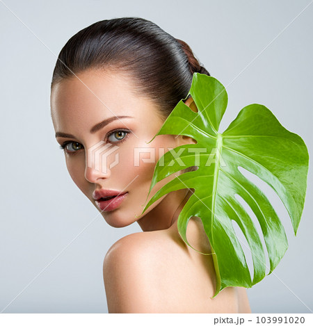 Beautiful woman with green leave near face and body. Closeup girl's face with green leave. Skin care beauty treatments concept. Beautiful woman with green leave near face and body. Closeup girl's face with green leave. Skin care beauty treatments concept. 103991020
