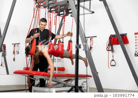 physical therapy, Physical rehabilitation, Health-improving exercises, doing exercises, decompression simulators. Rehabilitation exercises on red cord slings to restore pain-free movement patterns and physical therapy, Physical rehabilitation, Health-improving exercises, doing exercises, decompression simulators. Rehabilitation exercises on red cord slings to restore pain-free movement patterns and 103991774