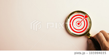 A magnifier glass highlights a target board for focused business objectives. With a background and copy space, it symbolizes the concept of search, goal achievement, and successful strategies. 103994035