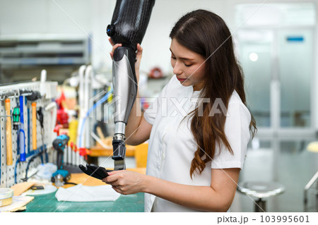 Female technician assembling and fixing parts of modern prosthetic leg 103995601