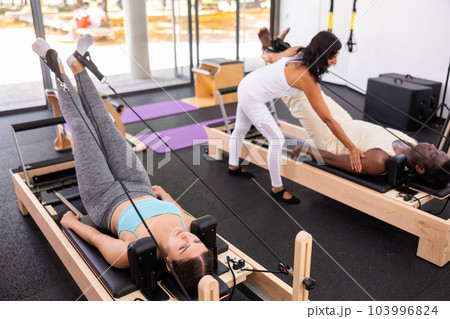 Active young Woman doing pilates exercises lying on pilates workout machines 103996824
