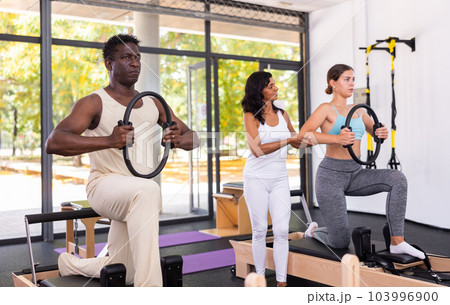 Man and woman doing exercises in pilates gym with man instructor 103996900