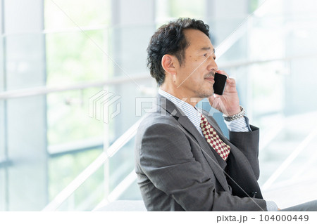 オフィスでスマホで話す中年ビジネスマン(上司・社長・リーダー) オフィスでスマホで話す中年ビジネスマン(上司・社長・リーダー) 104000449