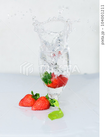 Strawberry fruit drops onto a wine glass, freeze motion of the water splash, white background. Strawberry fruit drops onto a wine glass, freeze motion of the water splash, white background. 104001211