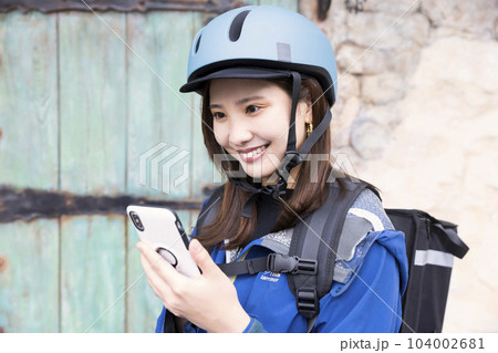 フードデリバリーイメージ デリバリー中スマホを確認する女性配達員 フードデリバリーイメージ デリバリー中スマホを確認する女性配達員 104002681