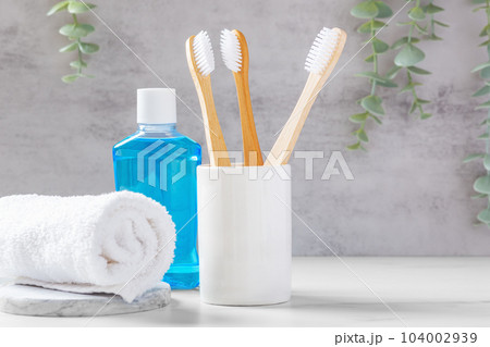 Bamboo toothbrushes in white cup with mouthwash and towel, dental care background Bamboo toothbrushes in white cup with mouthwash and towel, dental care background 104002939