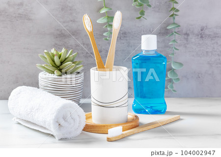 Dental care and dental hygiene concept, bamboo toothbrushes in cup with mouthwash and towel 104002947