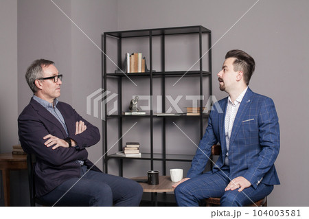 Mature successful businessman in glasses and blue suit discuss work with colleague in office 104003581
