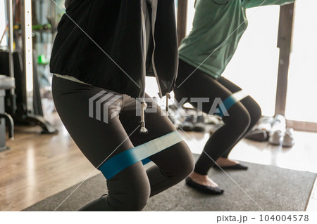 ジムでトレーニングチューブを使ってスクワットするアスリートの女性 104004578