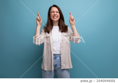 pretty brunette young female adult in shirt and jeans crossed fingers on blue background 104004688