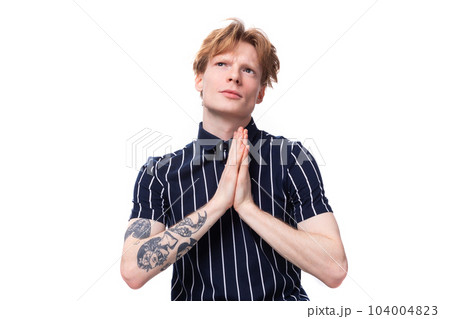 dreamy 25 year old blond man in striped polo praying on white background 104004823