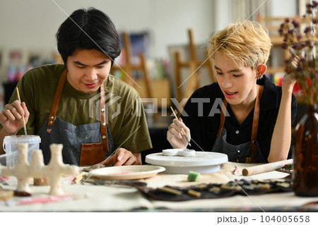 Handsome asian male ceramics art teacher helping a student with clay crafts in a pottery class. Art, handicraft and learning concept 104005658