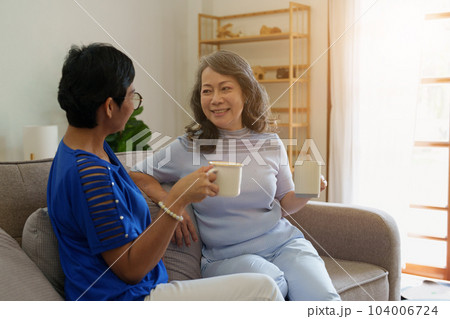 Asian elderly women talking together with friend sitting on sofa in living room at house 104006724