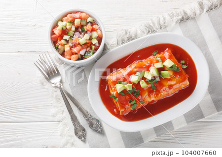 Tasty Wet Burritos with a beef, rice and refried bean filling wrapped in a tortilla smothered with red sauce closeup on the plate. Horizontal top view 104007660