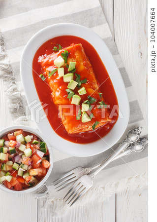 Wet Burrito stuffed with shredded meat, beans, rice and cheese, smothered in red enchilada sauce closeup on the plate. Vertical top view Wet Burrito stuffed with shredded meat, beans, rice and cheese, smothered in red enchilada sauce closeup on the plate. Vertical top view 104007664