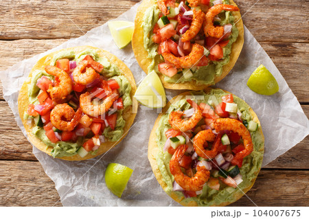 Freshly made shrimp tostadas topped with guacamole, onion, tomatoes, and cucumbers closeup on the table. Horizontal top view 104007675