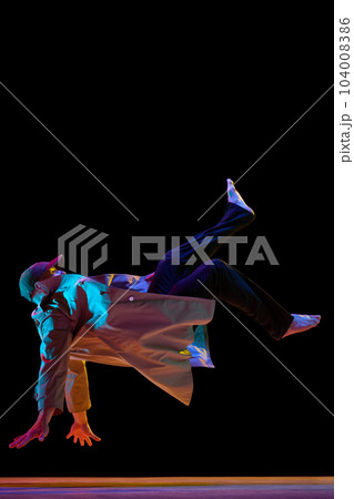 Dynamic image of young talented man in stylish clothes dancing breakdance, hip-hop against black studio background in neon light 104008386