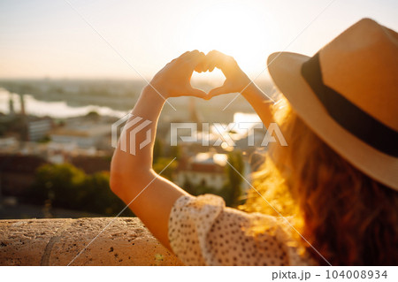 Woman tourist holding hands in shape of heart looking at panoramic landscape of city. Rest concept. 104008934