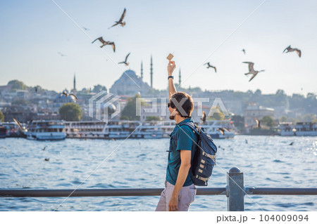 Young man traveler in pinc dress enjoying great view of the Bosphorus and lots of seagulls in Istanbul 104009094