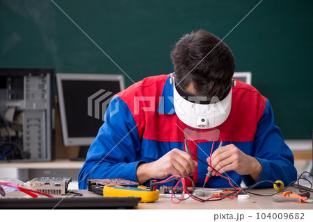 Young male repairman repairing computers in the classroom Young male repairman repairing computers in the classroom 104009682