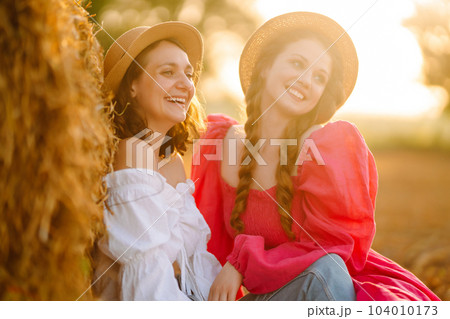 Two young women having fun near haystack. Fashion concept. Summer concept. Two young women having fun near haystack. Fashion concept. Summer concept. 104010173