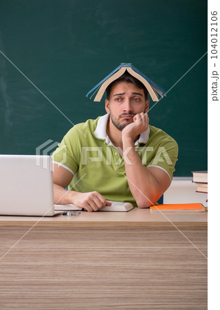 Young male student sitting in front of green board 104012106