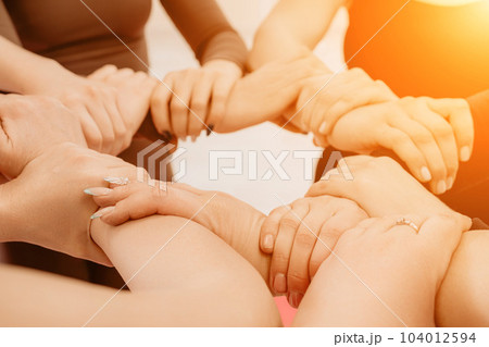 Partnership and unity concept: unrecognizable women in sportswear holding wrists of each other, forming circle. Group of happy young women holding hands. Side view on human hands. Partnership and unity concept: unrecognizable women in sportswear holding wrists of each other, forming circle. Group of happy young women holding hands. Side view on human hands. 104012594
