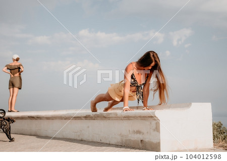 Woman park yoga. Side view of free calm bliss satisfied woman with long hair standing in morning park with yoga position against of sky by the sea. Healthy lifestyle outdoors in park, fitness concept. Woman park yoga. Side view of free calm bliss satisfied woman with long hair standing in morning park with yoga position against of sky by the sea. Healthy lifestyle outdoors in park, fitness concept. 104012598