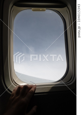 飛行機の窓から外を見る、窓枠に添えられた手の写真素材 [104015343