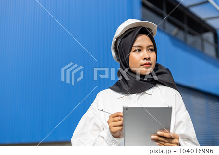 asian muslim woman industrial engineer in uniform wearing safety hard hat using tablet. 104016996