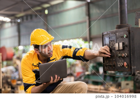 Industrial man engineer wear uniform and helmet using laptop are checking system machine at factory. 104016998