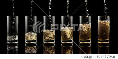Pouring yellow juice into a glass on a black background. 104017930