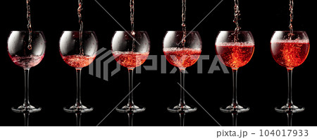 Pouring pink wine into a glass on a black background. Pouring pink wine into a glass on a black background. 104017933