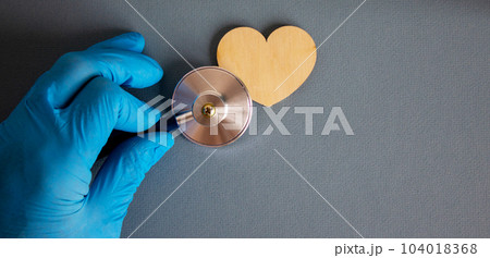 Wooden heart, hand in blue glove and stethoscope. 104018368