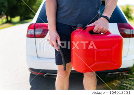 A man holds a red canister near a white car, close-up. Stop to refuel, no refueling, fuel problems. A man holds a red canister near a white car, close-up. Stop to refuel, no refueling, fuel problems. 104018551