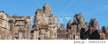 Capture of the ancient Bayon Temple in Cambodia, with its iconic stone towers featuring human faces, on a sunny day. 104019124
