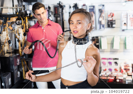 Girl and man choosing black collar in sex shop 104019722
