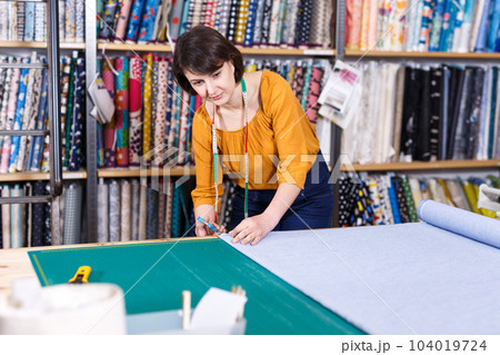 Female seller measuring and cutting off piece of textile 104019724