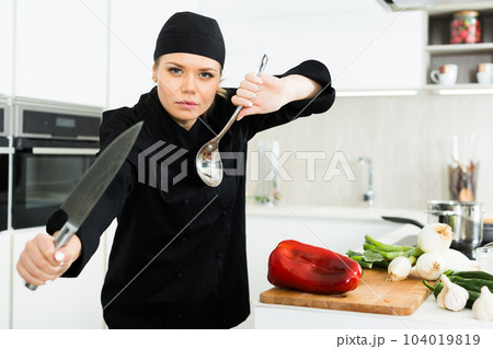 Young woman chef in black uniform posing with big knife 104019819