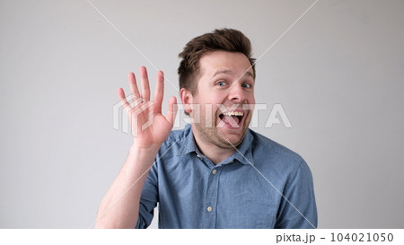 European young man waves his hand, greets his friends. 104021050