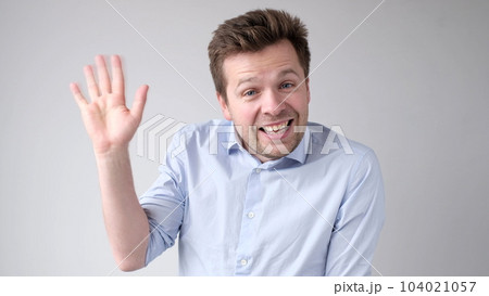 European young man waves his hand, greets his friends. 104021057