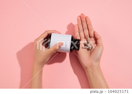 Against a pink background, some capsules are poured into a hand from a medicine box. Medicines can treat diseases and improve your health 104025171