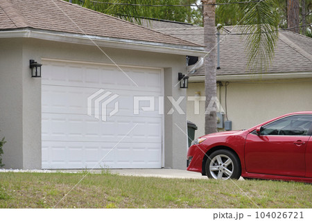 Vehicle parked in front of wide garage double door on paved driveway of typical contemporary american home 104026721