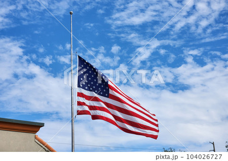 USA national flag waving lowered to half mast on wind against blue sky. American stars and stripes spangled banner as symbol of democracy 104026727