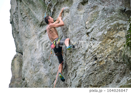Strong male climber climbing steep wall of rocky mountain. Sportsman overcoming difficult route. Engaging in extreme sports hobby concept. Strong male climber climbing steep wall of rocky mountain. Sportsman overcoming difficult route. Engaging in extreme sports hobby concept. 104026847
