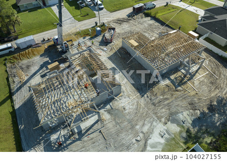 Professional builders and crane truck working on roof construction of unfinished suburban home with wooden frame structure in Florida rural area. Concept of housing development in America Professional builders and crane truck working on roof construction of unfinished suburban home with wooden frame structure in Florida rural area. Concept of housing development in America 104027155